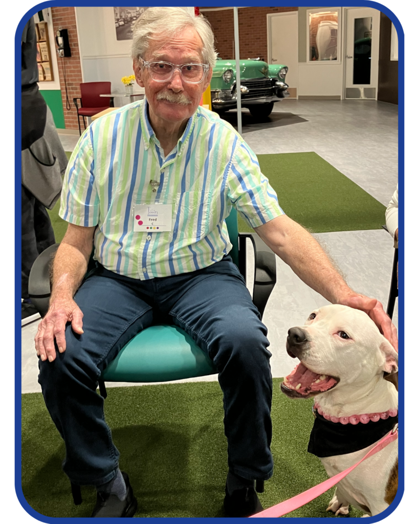 Senior man sitting with a friendly dog during a social event at Town Square NW Austin, showcasing the importance of pet therapy and social connections for emotional and mental health in older adults.